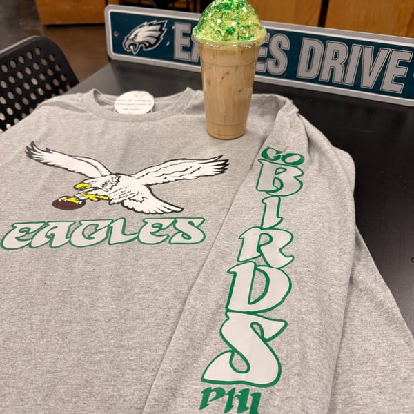 Gray Eagles long-sleeve shirt with a green-topped iced coffee and an "Eagles Drive" sign.