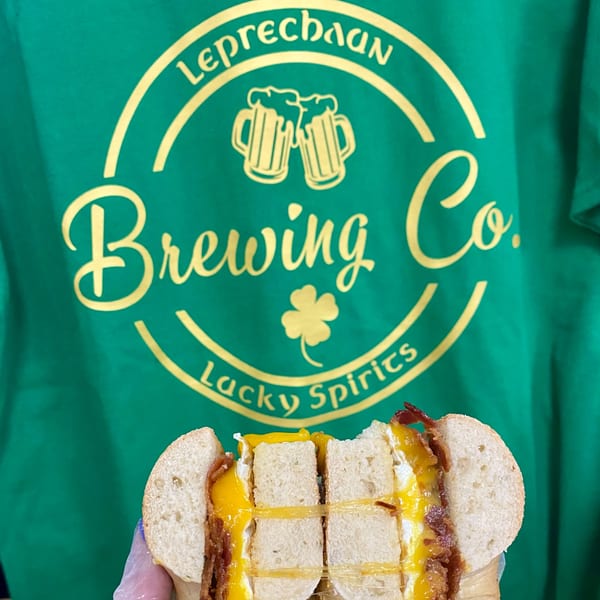 A Redhouse Bagels breakfast sandwich with egg, cheese, and bacon, held against a green t-shirt.