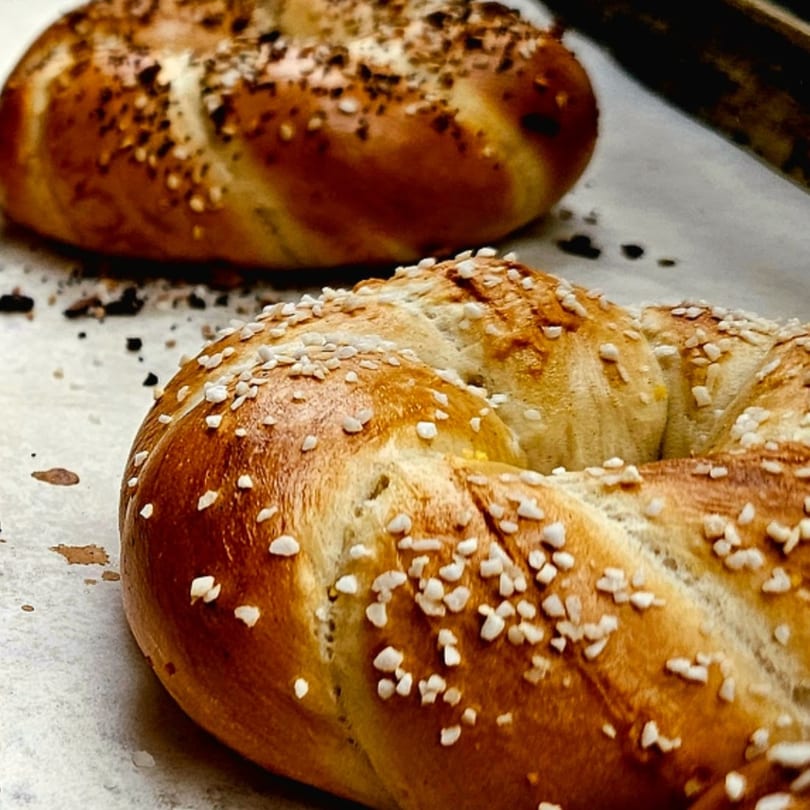 Two freshly baked, golden-brown bagels, one topped with salt and the other with everything seasoning.