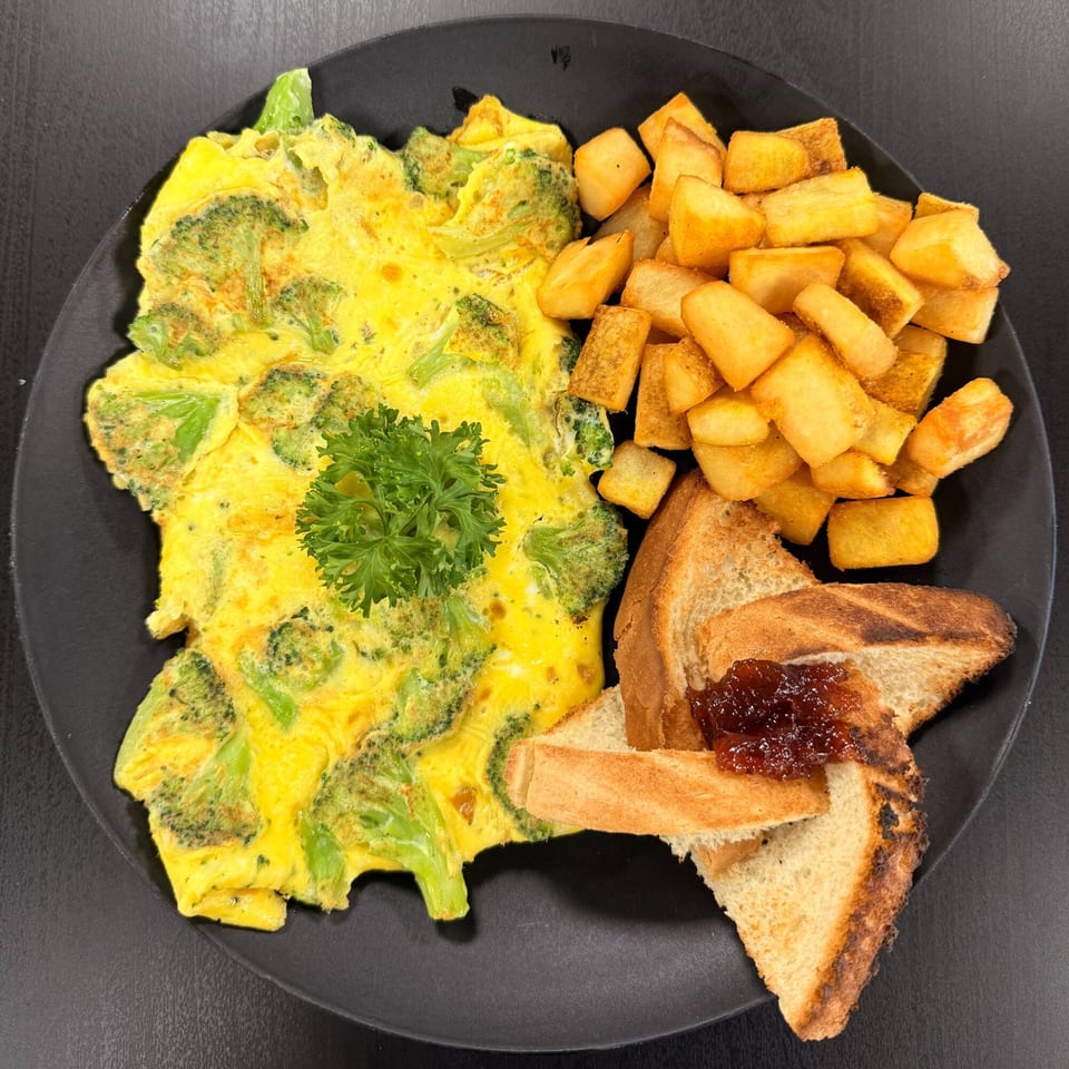 Broccoli omelet with home fries and toast with jam on a black plate.