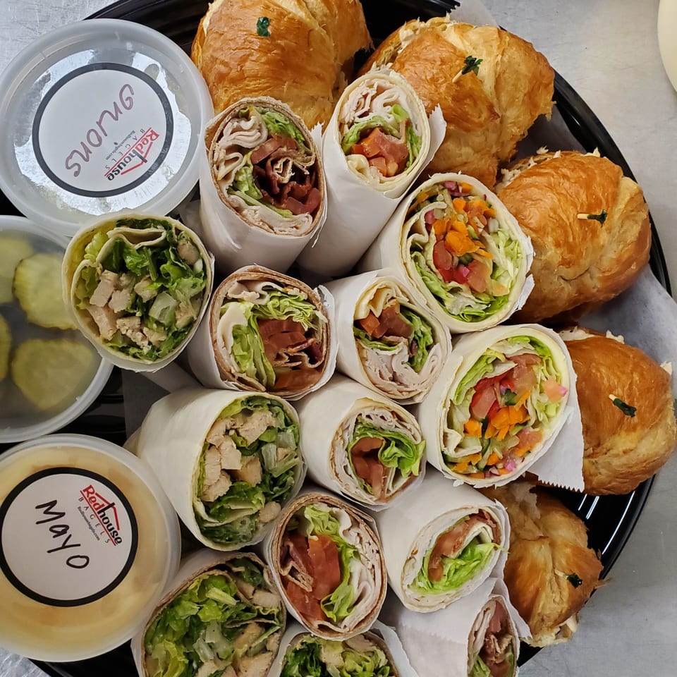 Catering tray with assorted wraps, croissants, pickles, and containers of mayo and onions from Redhouse Bagels.