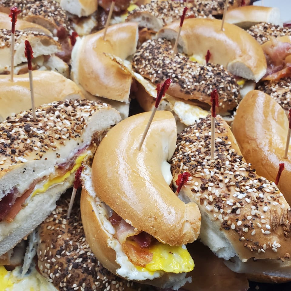 Close-up of numerous Redhouse Bagels breakfast sandwiches with egg and bacon, held together by toothpicks.