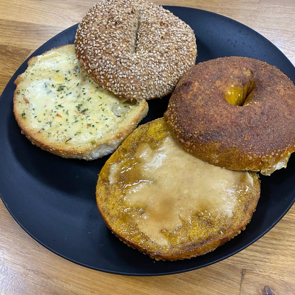 A black plate holds two Redhouse Bagels, one sesame and one cinnamon, with cream cheese spreads.