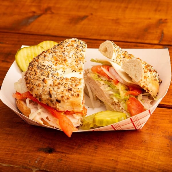Everything bagel sandwich with turkey, cheese, lettuce, tomato, and onion, served with pickles.