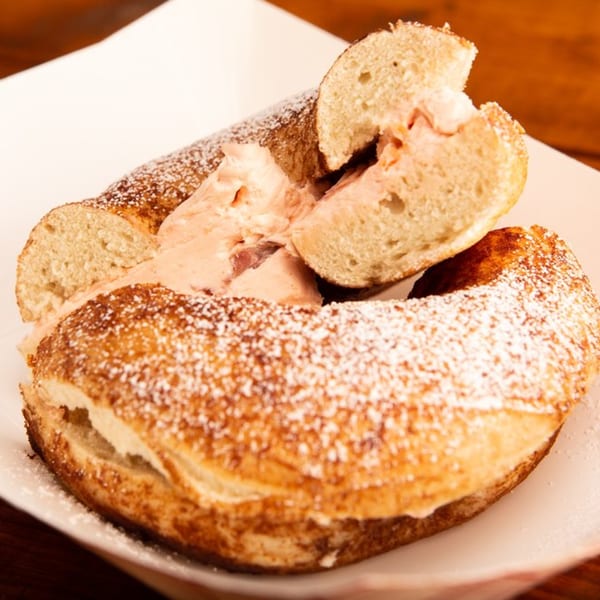 A Redhouse Bagels cinnamon sugar bagel, split and filled with strawberry cream cheese, dusted with powdered sugar.
