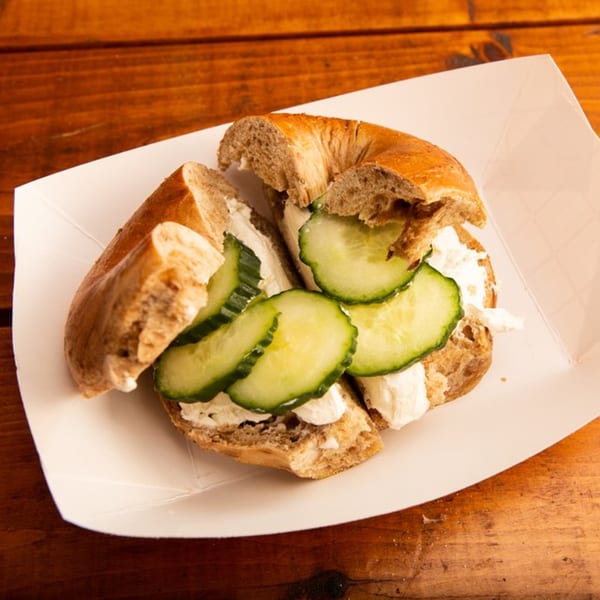 A Redhouse Bagels bagel with cream cheese and cucumber slices in a white paper tray.