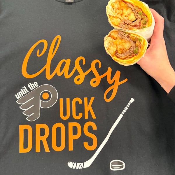 Hand holding a breakfast burrito, cut in half, over a black t-shirt with orange text.