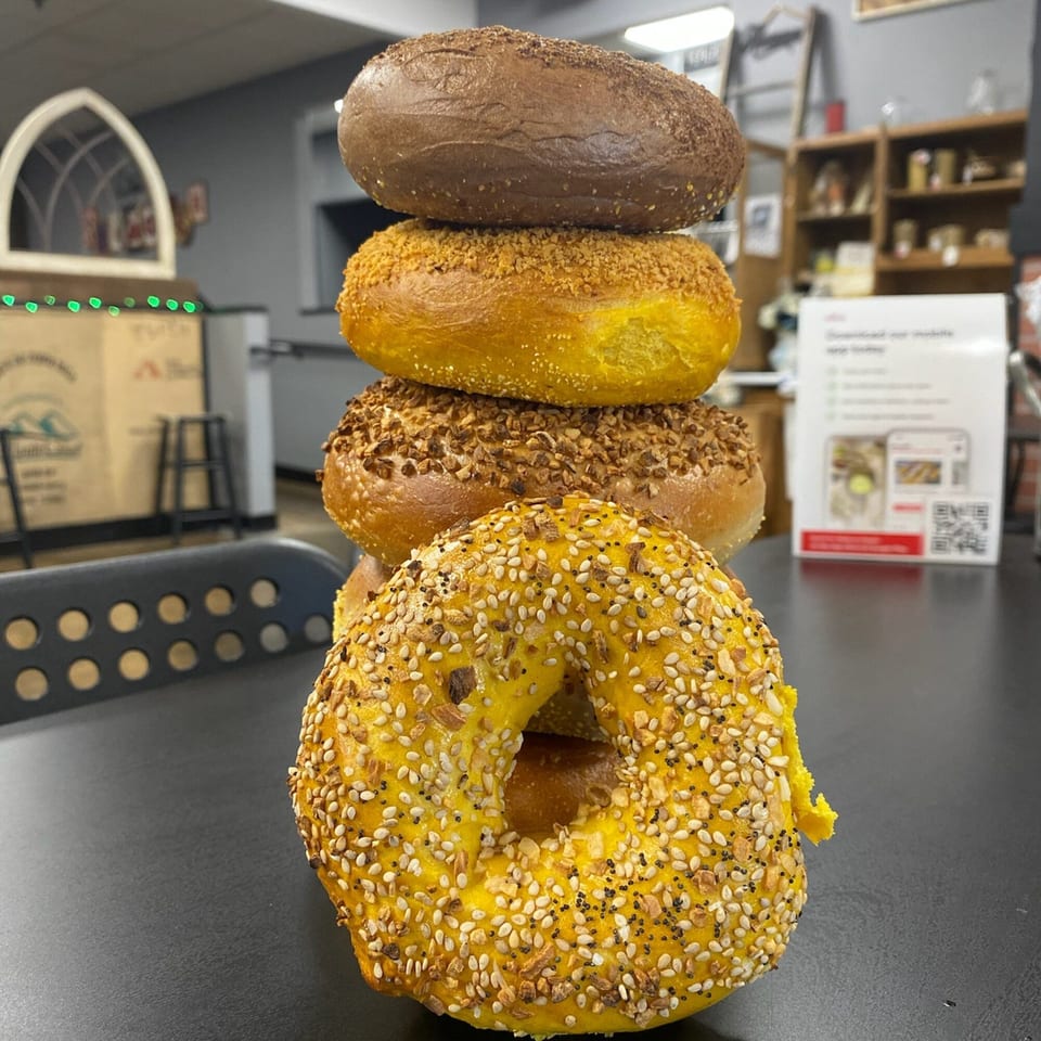 A stack of five Redhouse Bagels, including chocolate, onion, and everything varieties, on a black table.